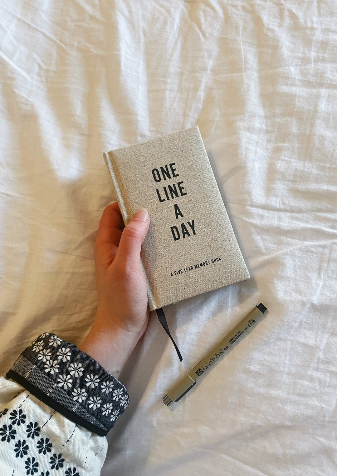 One Line a Day journal laying on a bed with a pen.