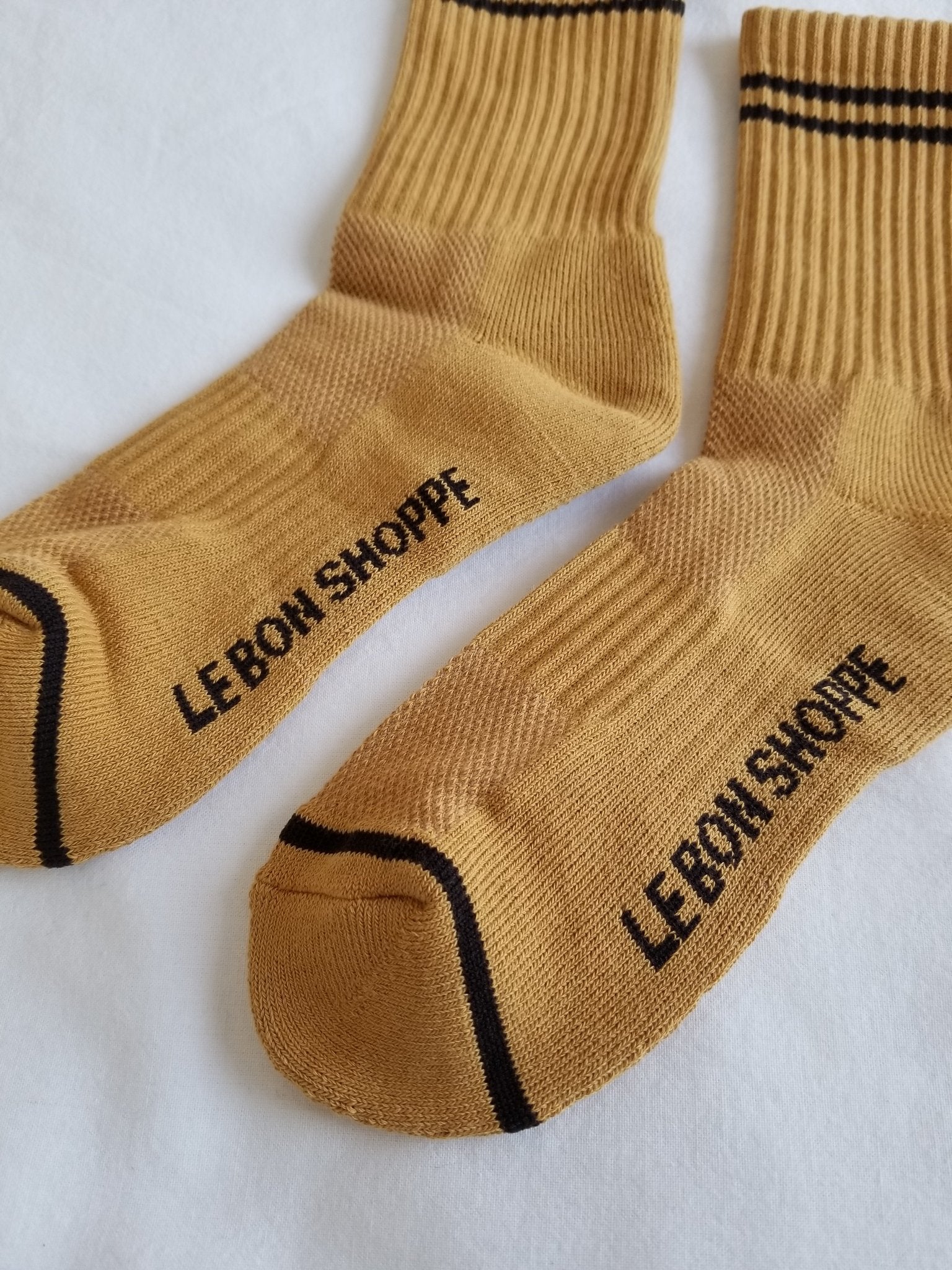 Close up of gold colored socks with navy stripes on a white background.