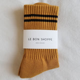 Gold colored socks with navy stripes in Le Bon Shoppe packaging on a white background.