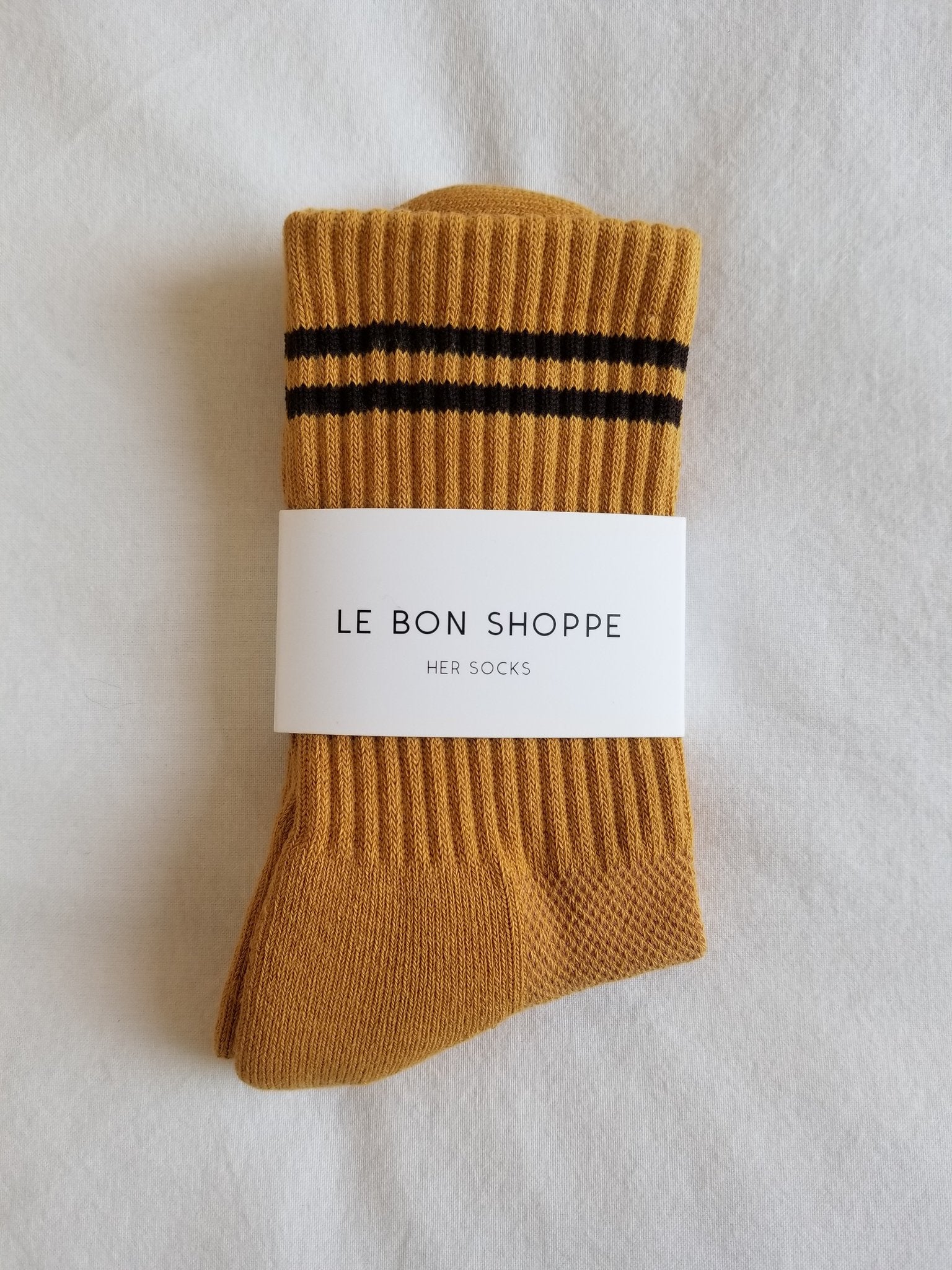 Gold colored socks with navy stripes in Le Bon Shoppe packaging on a white background.