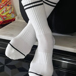 A pair of white socks with black double stripes on the cuffs, displayed on a surface.