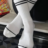 A pair of white socks with black double stripes on the cuffs, displayed on a surface.