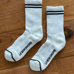 White socks with black stripes on the cuff and Le Bon Shoppe branding on wood surface.