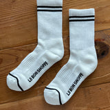 White socks with black stripes on the cuff and Le Bon Shoppe branding on wood surface.