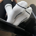 Person wearing white socks with black stripes and black leggings with their feet on a railing.