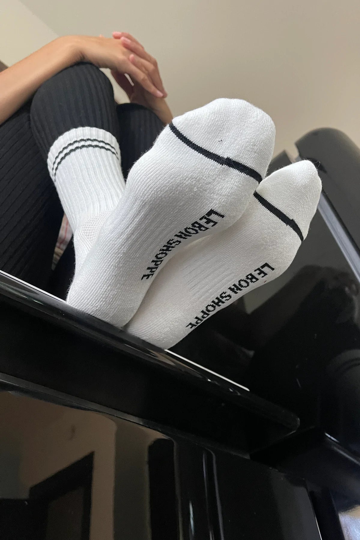 Person wearing white socks with black stripes and black leggings with their feet on a railing.