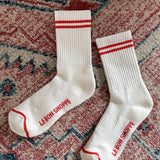 White socks with red stripes laying on a red printed rug.