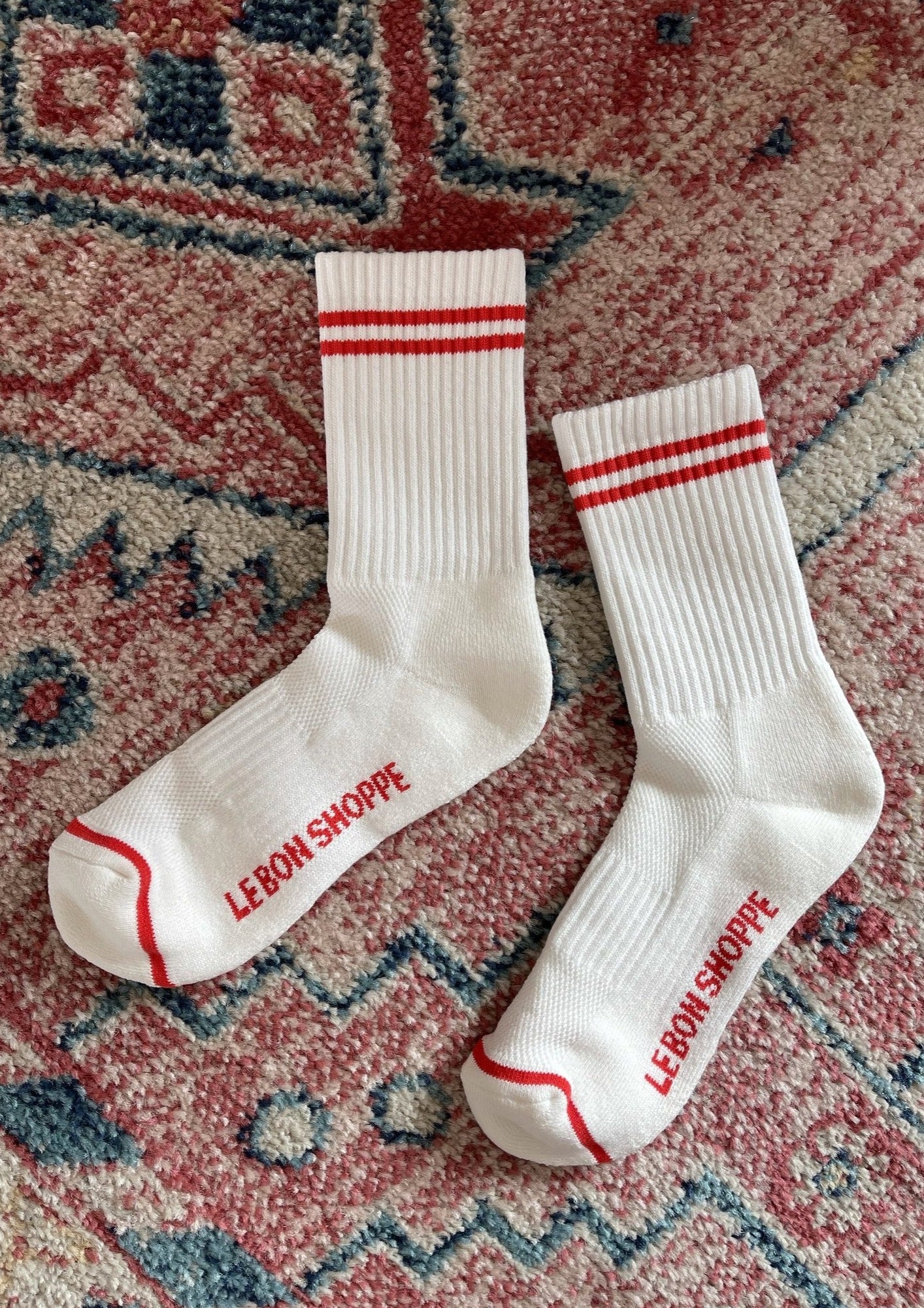 White socks with red stripes laying on a red printed rug.