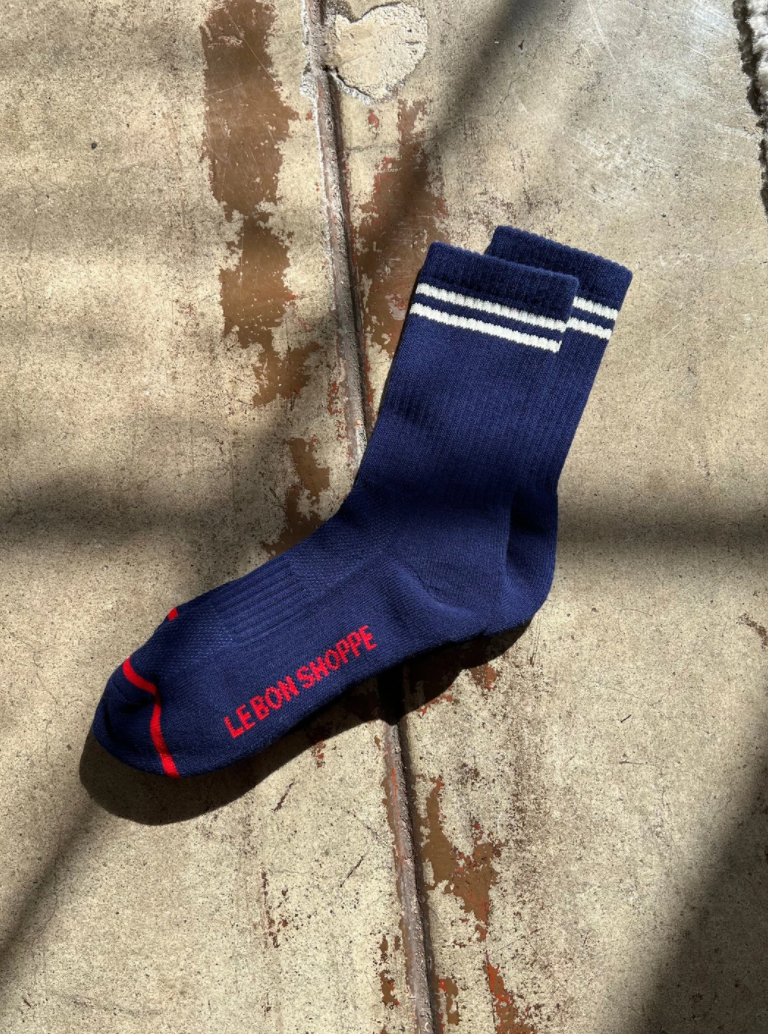 Navy socks with white stripes and red Le Bon Shoppe branding on a wood surface.
