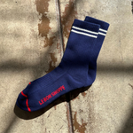 Navy socks with white stripes and red Le Bon Shoppe branding on a wood surface.