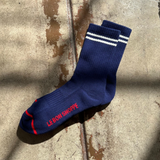 Navy socks with white stripes and red Le Bon Shoppe branding on a wood surface.