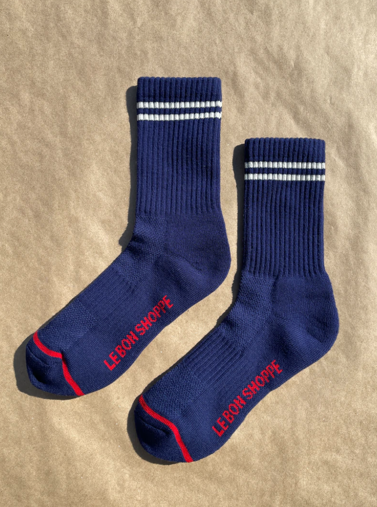 Navy socks with white stripes on the cuff and red Le Bon Shoppe branding on a kraft paper surface.
