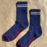 Navy socks with white stripes on the cuff and red Le Bon Shoppe branding on a kraft paper surface.