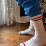 A pair of calf-length white socks with red and blue stripes on the cuffs, worn with blue sweatpants.