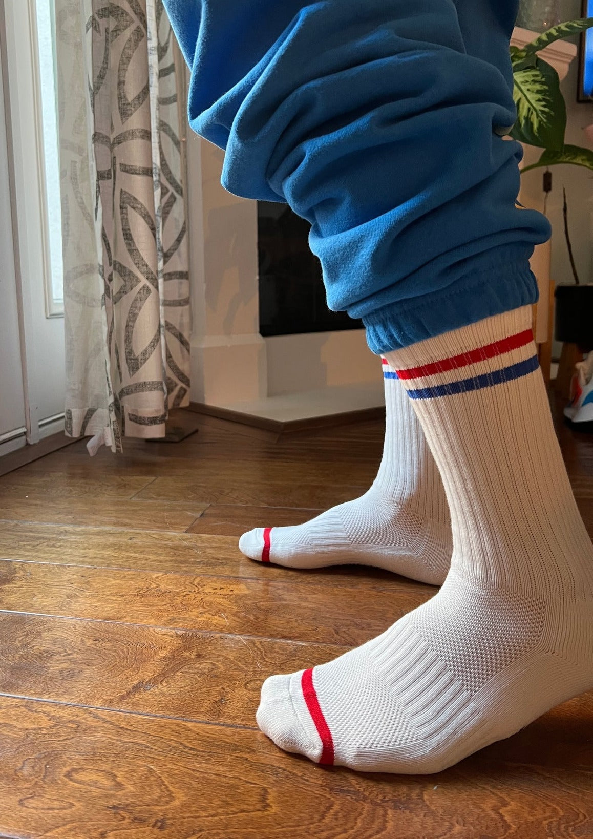 A pair of calf-length white socks with red and blue stripes on the cuffs, worn with blue sweatpants.