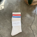 White socks with blue and red stripe in white Le Bon Shoppe packaging on concrete floor
