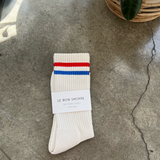White socks with blue and red stripe in white Le Bon Shoppe packaging on concrete floor