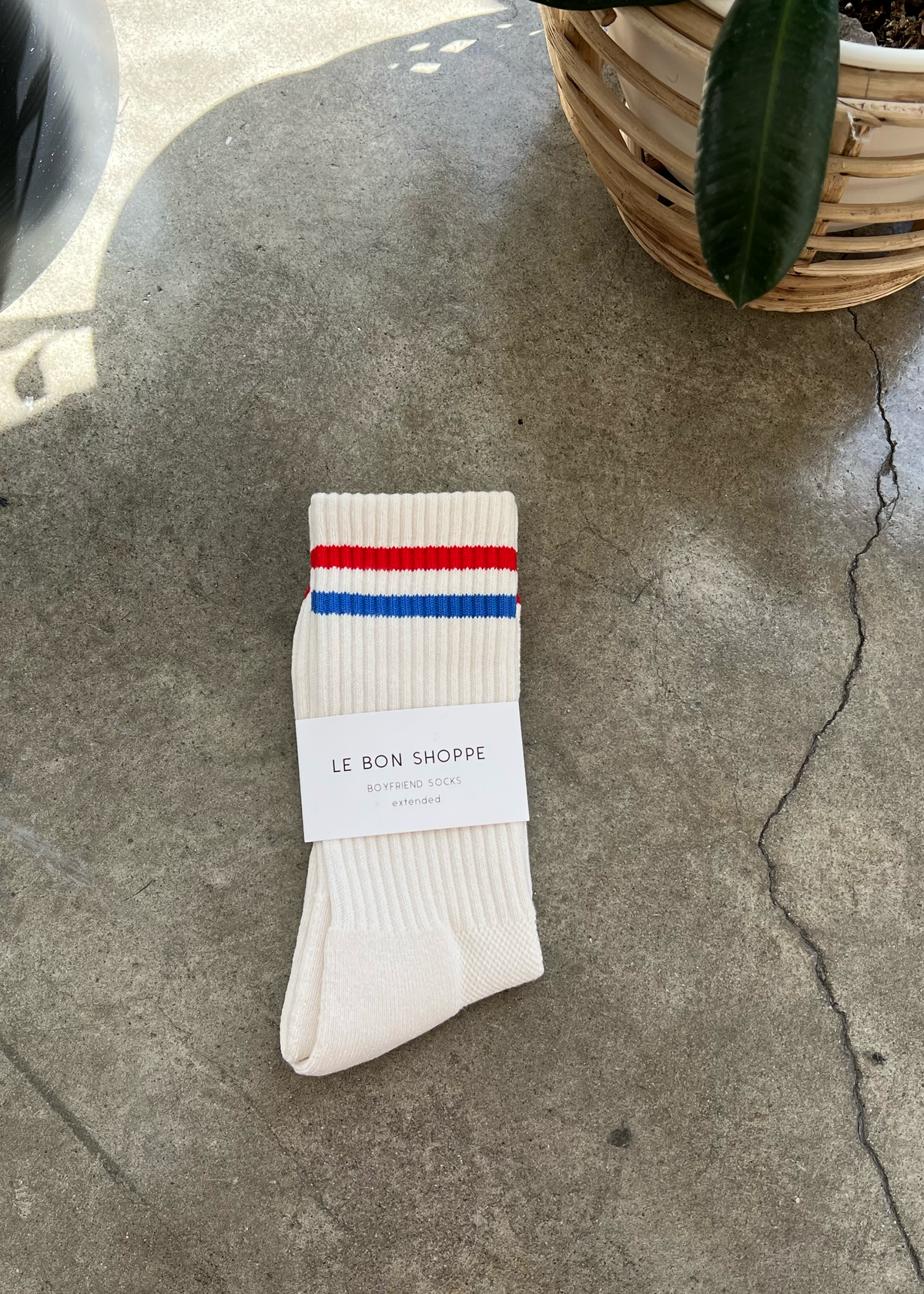 White socks with blue and red stripe in white Le Bon Shoppe packaging on concrete floor