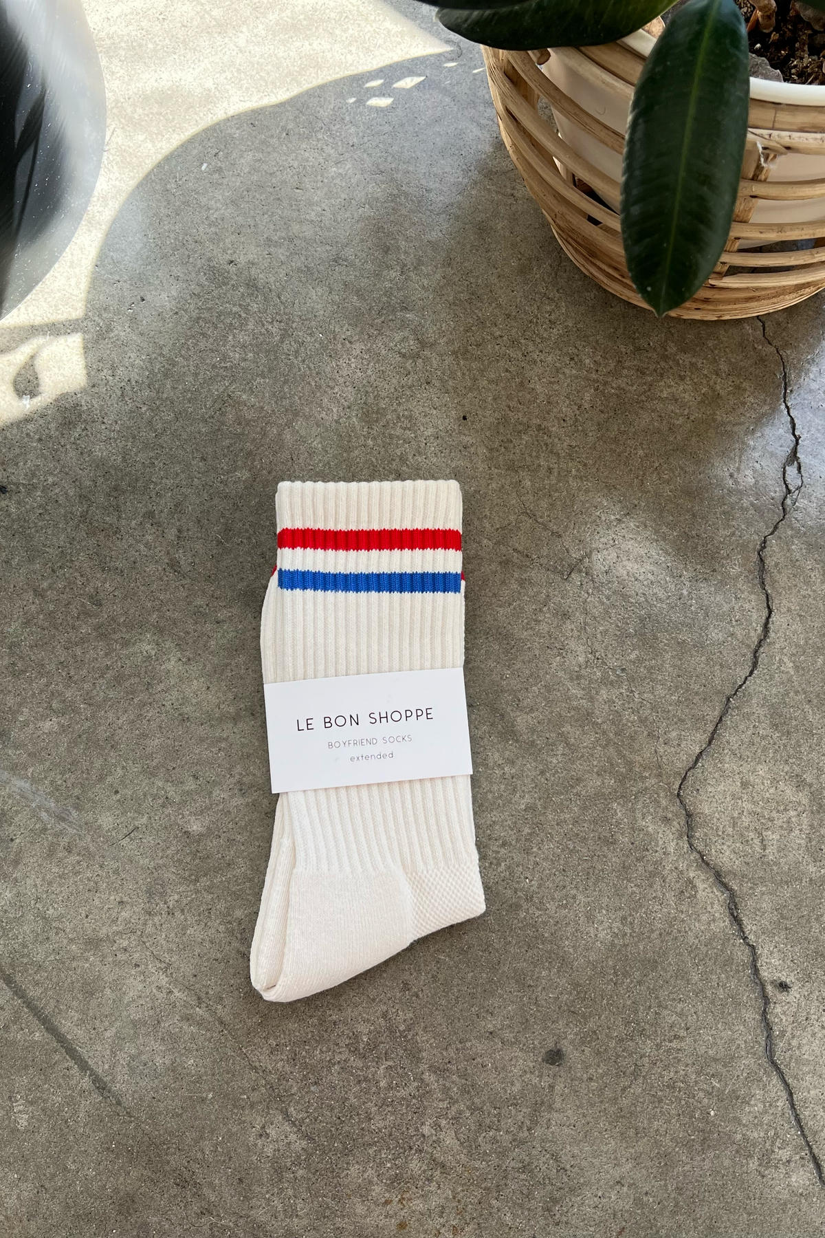 White socks with blue and red stripe in white Le Bon Shoppe packaging on concrete floor