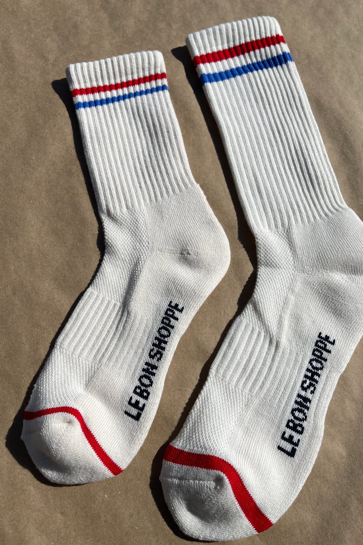White socks with blue and red socks and e Bon Shoppe branding laying on kraft paper