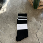 Black socks with white stripes in white packaging on concrete floor