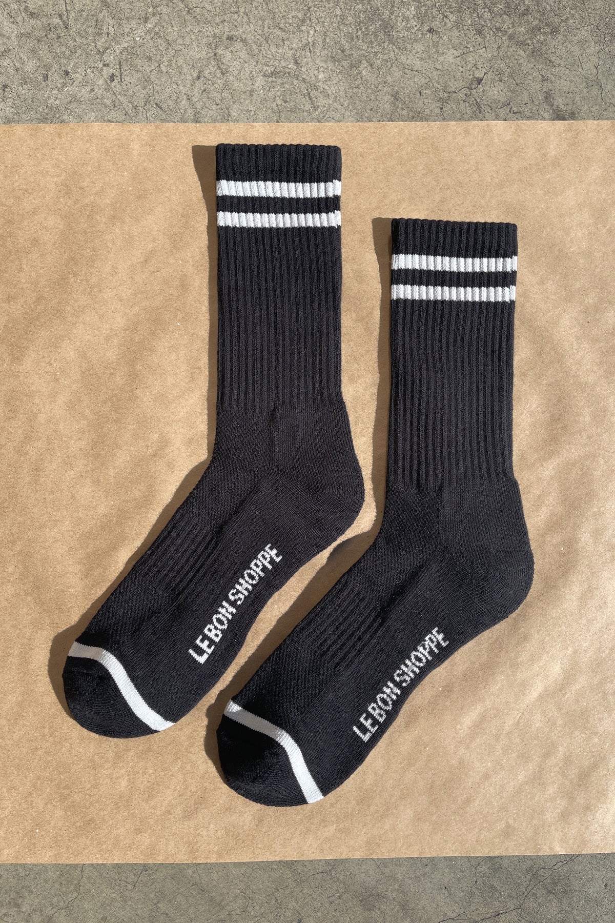 Black socks with white stripes and Le Bon Shoppe branding on kraft paper background
