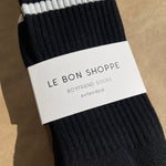 Black socks with white stripes in Le Bon Shoppe branding packaging on kraft paper background