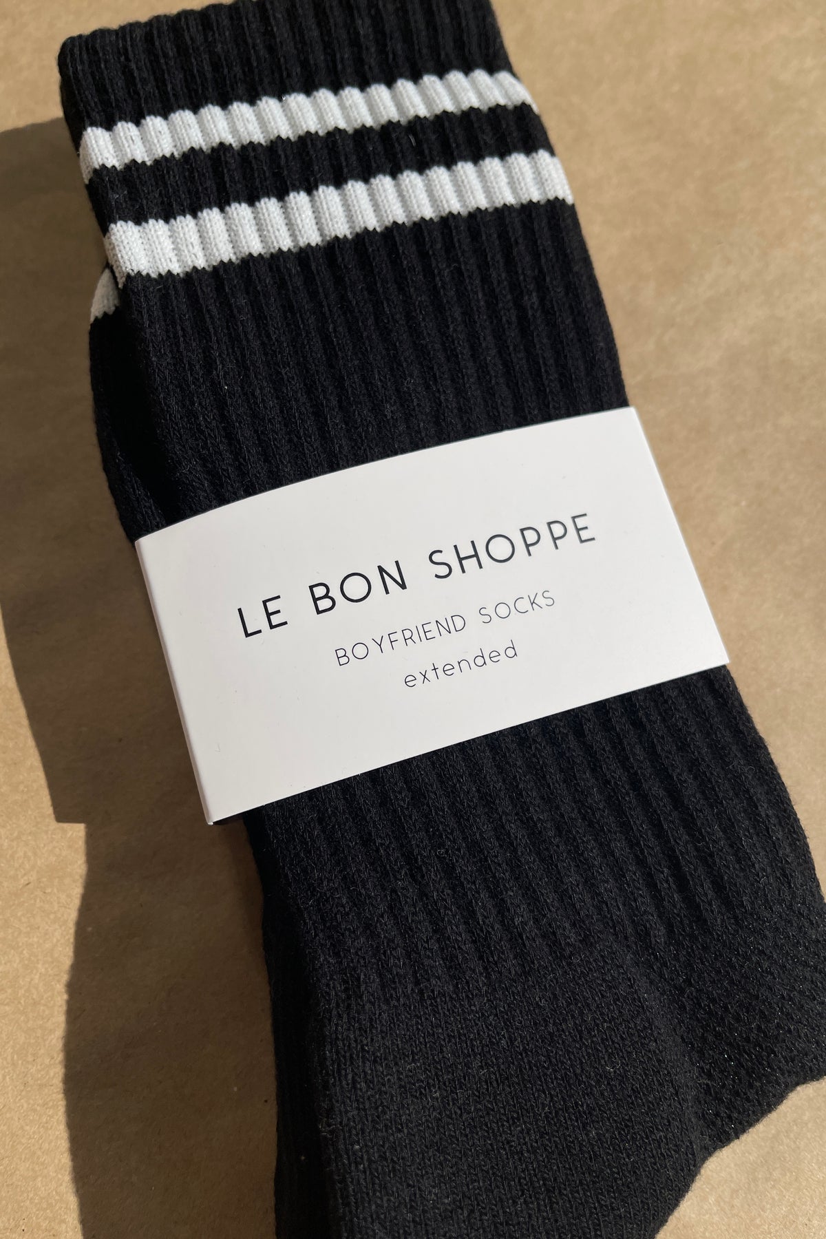 Black socks with white stripes in Le Bon Shoppe branding packaging on kraft paper background