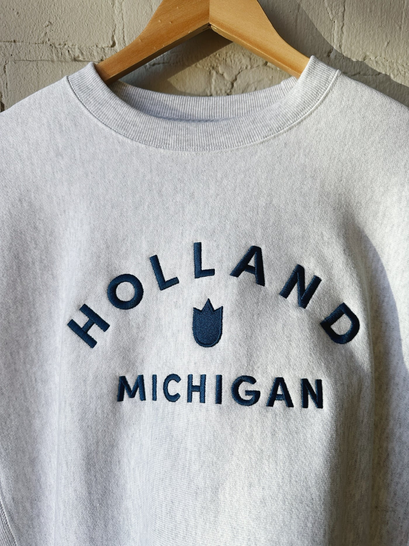 A heather grey crewneck sweatshirt with Holland Michigan and a tulip in navy embroidered on it.
