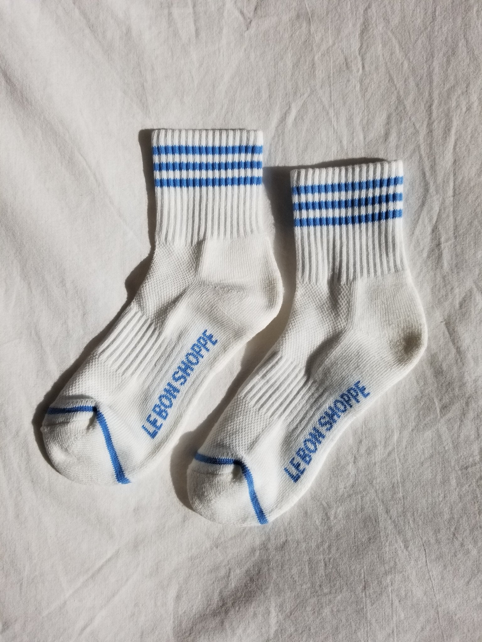 White socks with blue stripes and Le Bon Shoppe branding on white background