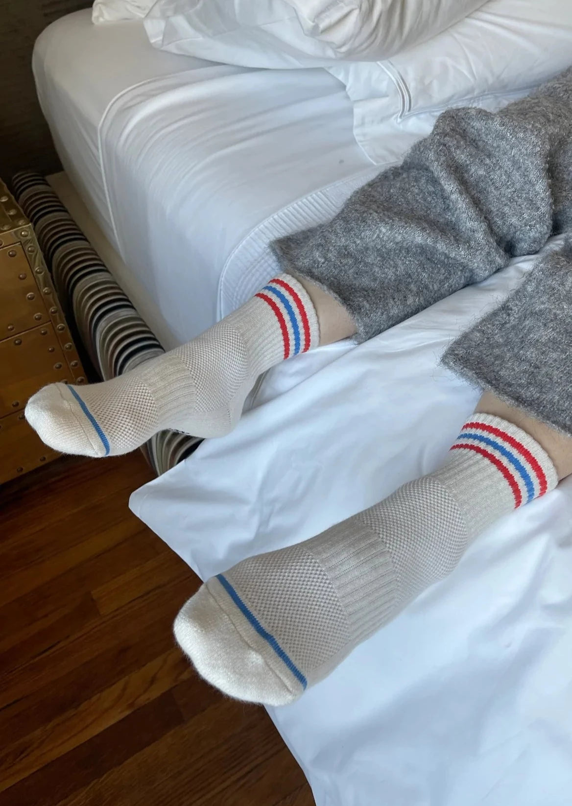 A pair of socks with a white base and red and blue stripes at the cuff, worn on an individual lying on a bed.