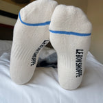 Bottom of person's feet wearing white socks with blue stripe and Le Bon Shoppe branding on white sheets