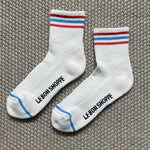 White Le Bon Shoppe socks with red and blue stripes laying on textured carpet