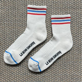 White Le Bon Shoppe socks with red and blue stripes laying on textured carpet