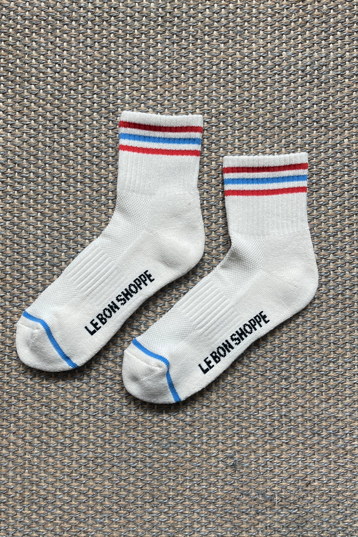 White Le Bon Shoppe socks with red and blue stripes laying on textured carpet