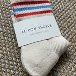 White Le Bon Shoppe socks with red and blue stripes laying on textured carpet