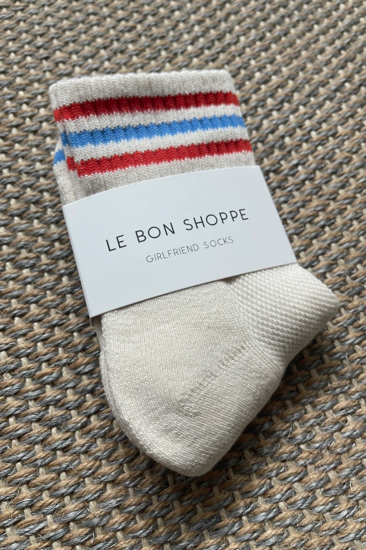 White Le Bon Shoppe socks with red and blue stripes laying on textured carpet
