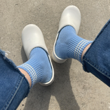 A pair of blue ankle crew socks with a triple contrast stripe at the opening, worn with denim jeans and white clogs.