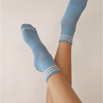 Person's legs wearing blue socks with white stripes in front of light grey background
