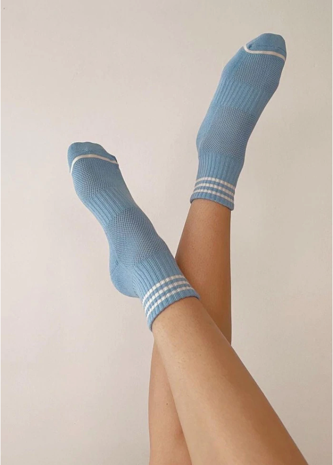 Person's legs wearing blue socks with white stripes in front of light grey background