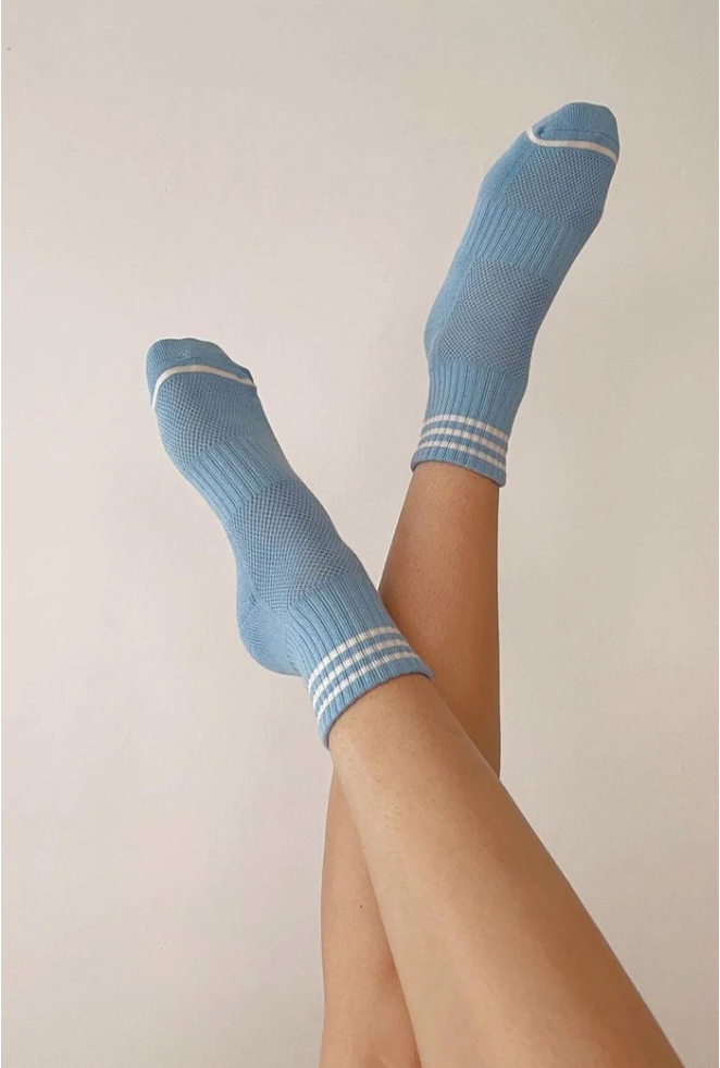 Person's legs wearing blue socks with white stripes in front of light grey background