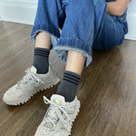 Person wearing gray ankle crew socks with a triple contrast stripe at the opening, paired with blue jean overalls and beige sneakers.