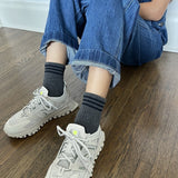 Person wearing gray ankle crew socks with a triple contrast stripe at the opening, paired with blue jean overalls and beige sneakers.