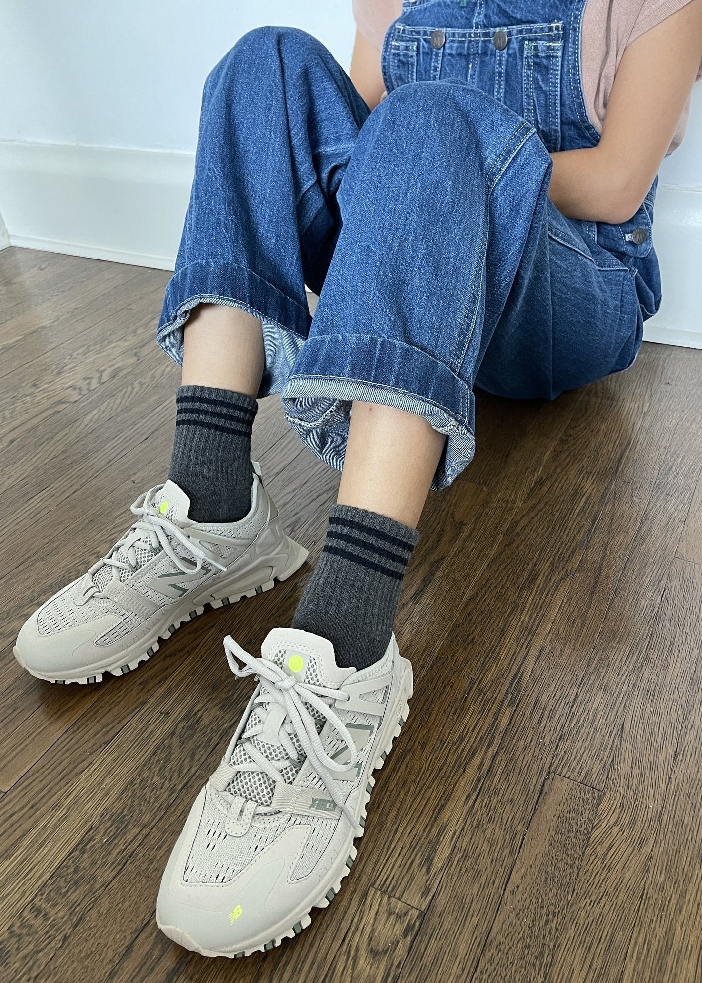 Person wearing gray ankle crew socks with a triple contrast stripe at the opening, paired with blue jean overalls and beige sneakers.