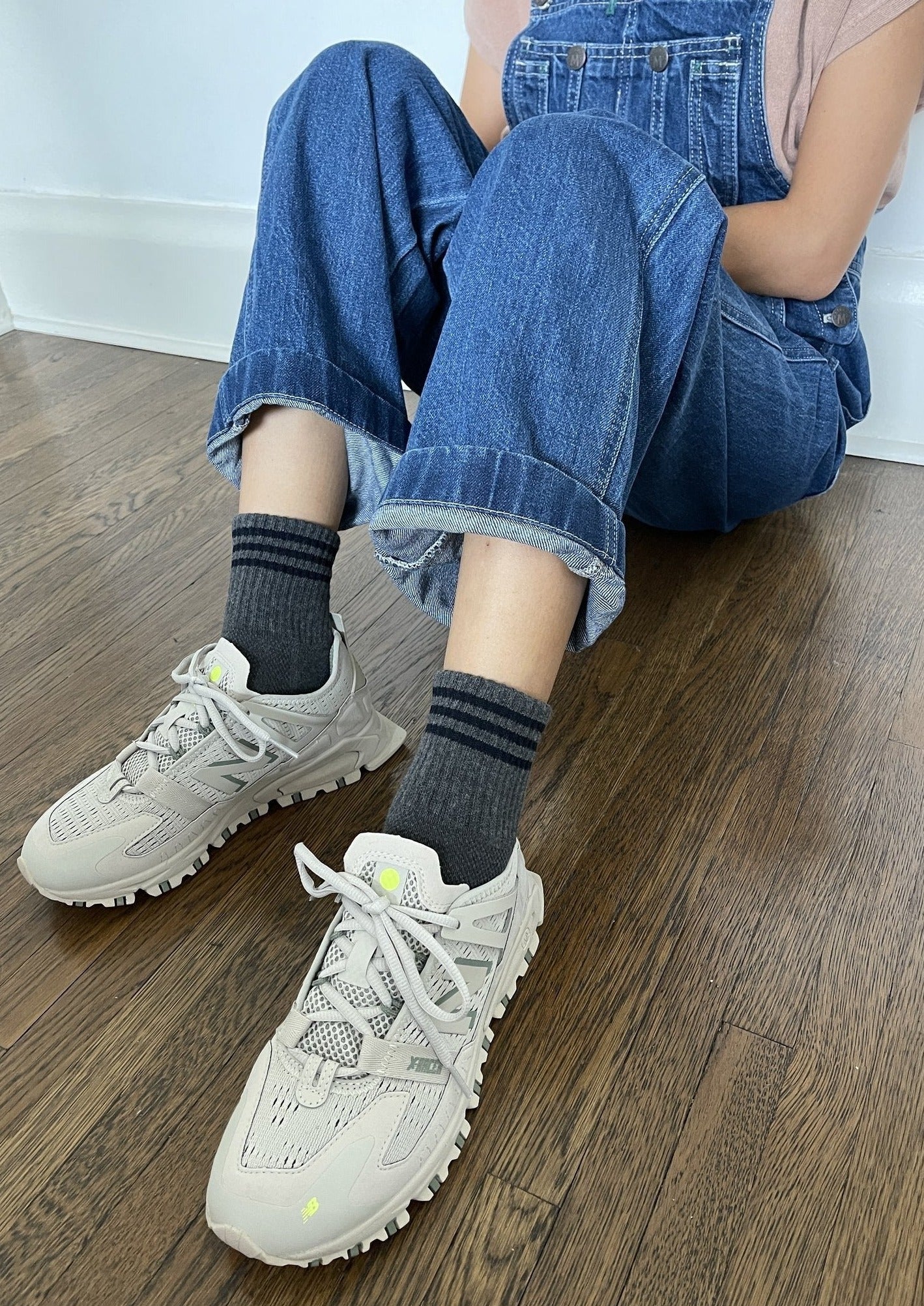 Person wearing gray ankle crew socks with a triple contrast stripe at the opening, paired with blue jean overalls and beige sneakers.
