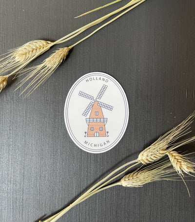 Oval sticker laying on a black background with wheat strands on it.Sticker displays a windmill with the words Holland Michigan on it