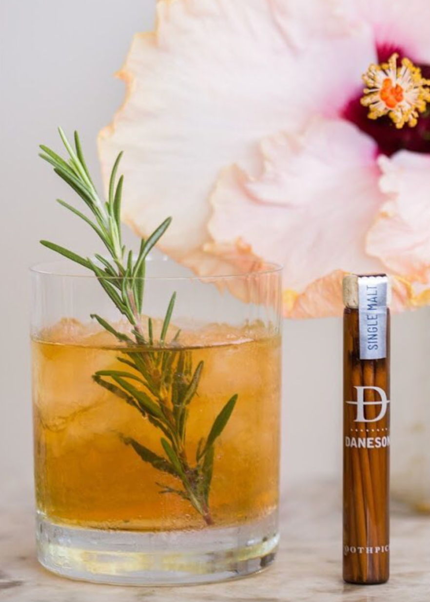 A set of flavored toothpicks in a glass jar next to a cocktail.