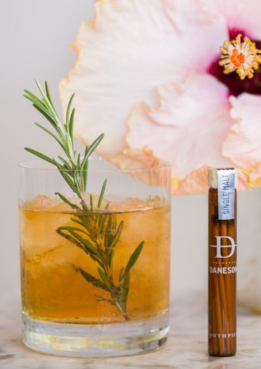 A set of flavored toothpicks in a glass jar next to a cocktail.