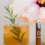 A set of flavored toothpicks in a glass jar next to a cocktail.