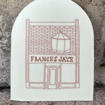A cream colored arched sticker with Frances Jaye store front etched on it.
